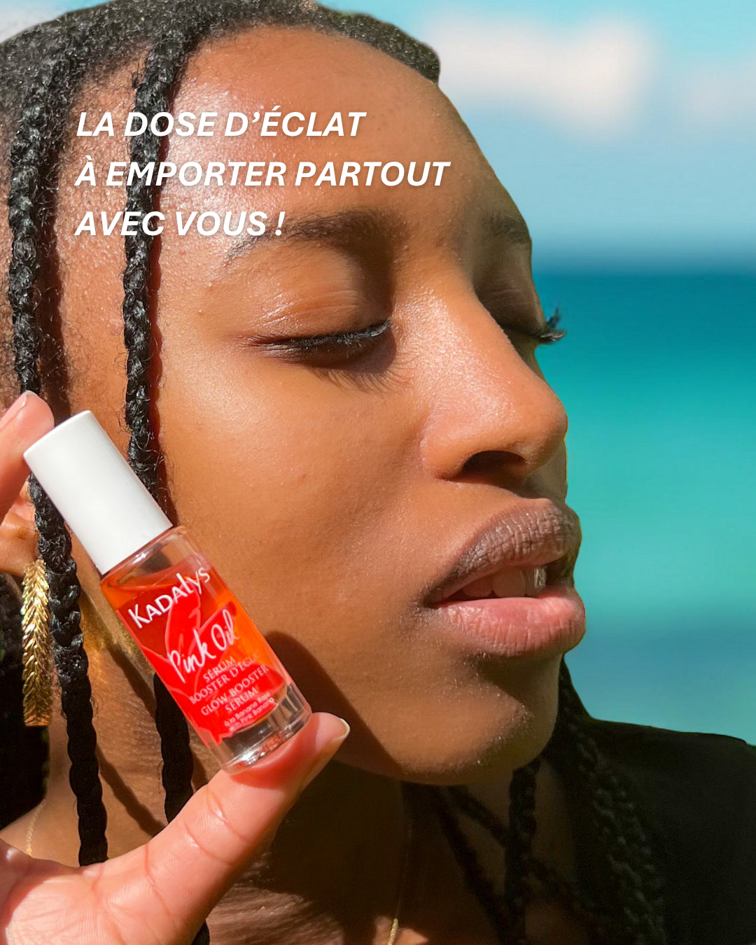 Femme tenant le sérum booster d'éclat Pink Oil Kadalys format voyage devant une plage, idéal pour emporter votre soin visage éclat partout avec vous.